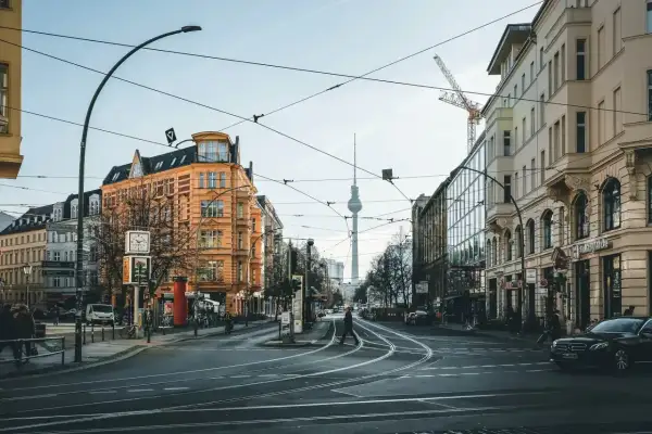 Skrzyżowanie w Berlinie z widoczną wieżą telewizyjną. Czy Berlin jest bezpieczny? Widać ludzi spacerujących, tramwaje i samochody.
