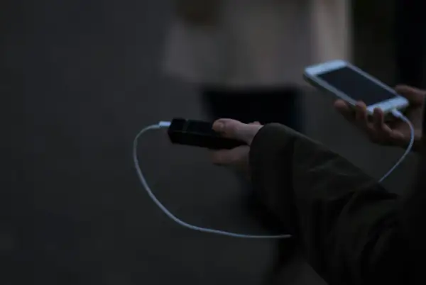 Ręka trzyma powerbank i smartfon, podłączone kablem. Elektronika w samolocie to klucz do rozrywki podczas podróży.