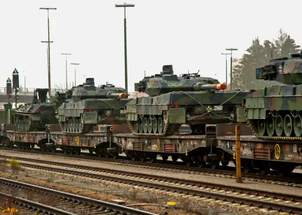 Pociąg wojskowy transportuje kilka czołgów Leopard 2 na wagonach platformach.