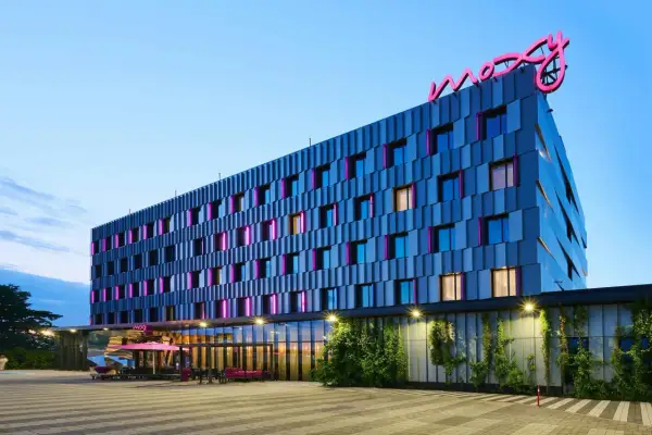 Nowoczesny hotel Moxy Hotels Pyrzowice z neonowym logo na dachu i kolorowymi podświetleniami okien.