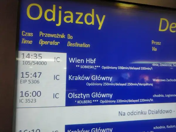 Tablica odjazdów pociągów pokazuje, jak sprawdzić opóźnienie pociągu. Widać opóźnione pociągi do Wiednia, Krakowa i Olsztyna.