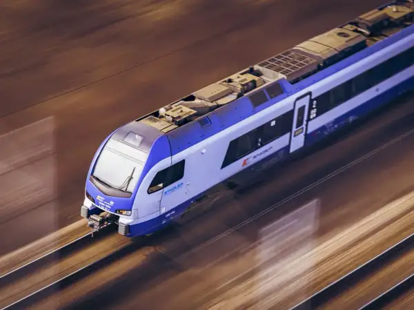 Nowoczesny pociąg Stadler FLIRT, z charakterystycznym niebiesko-białym malowaniem, pędzi po torach. To może być pociąg zamoyski, który zabiera pasażerów w podróż.